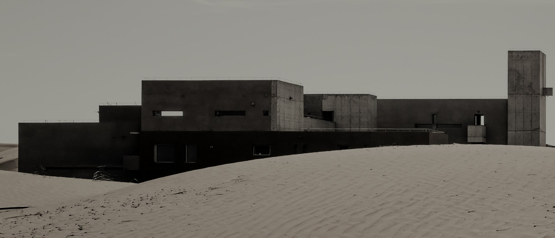Concrete volumes and a tall water tower rising from rolling sand dunes.