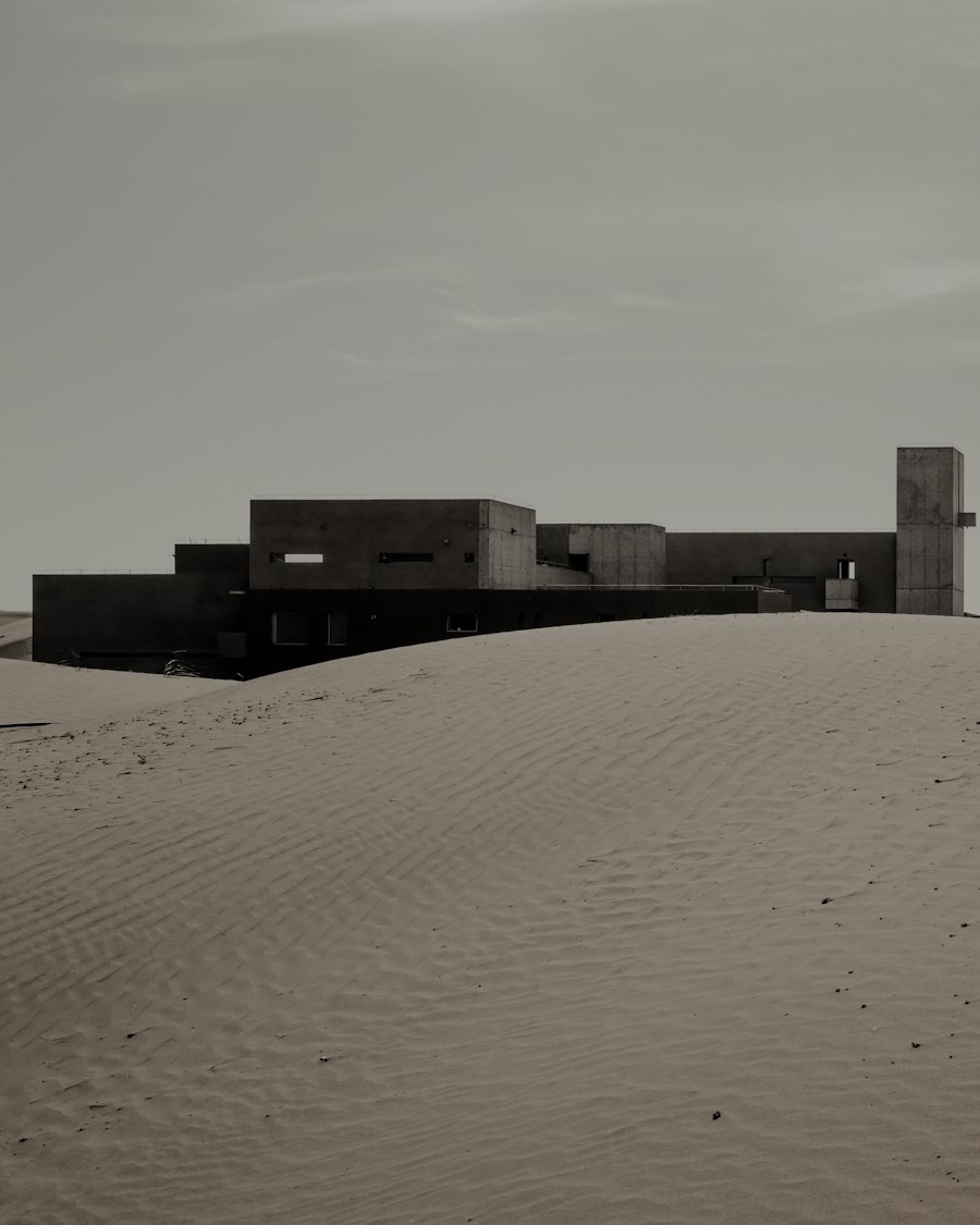 Concrete volumes and a tall water tower rising from rolling sand dunes.