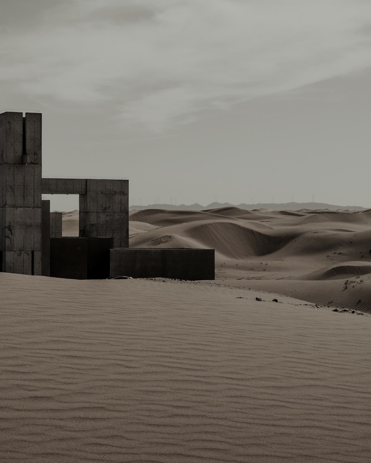 Concrete volumes and a tall water tower rising from rolling sand dunes.