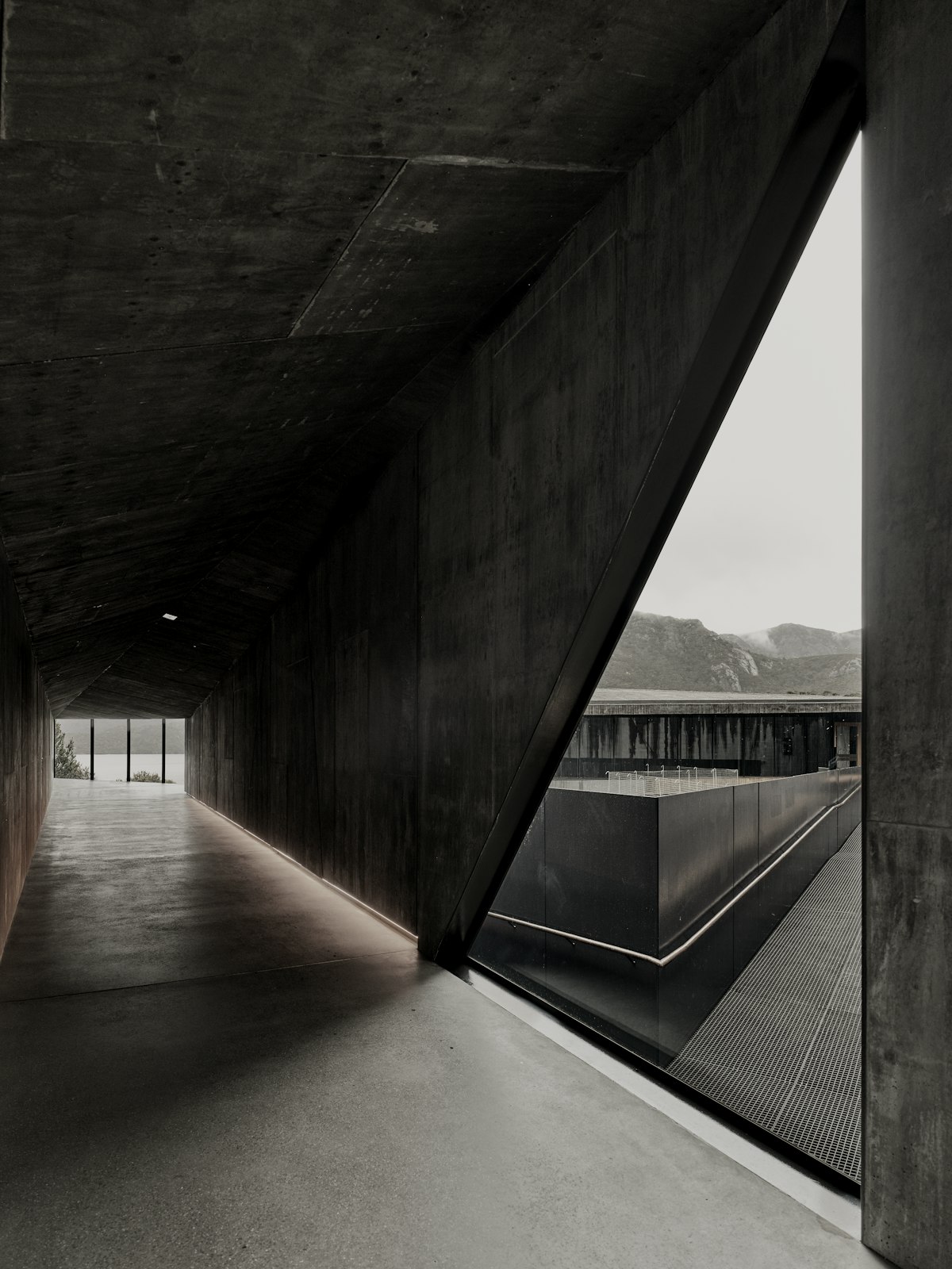 A concrete corridor lit by a triangular window over a pool.
