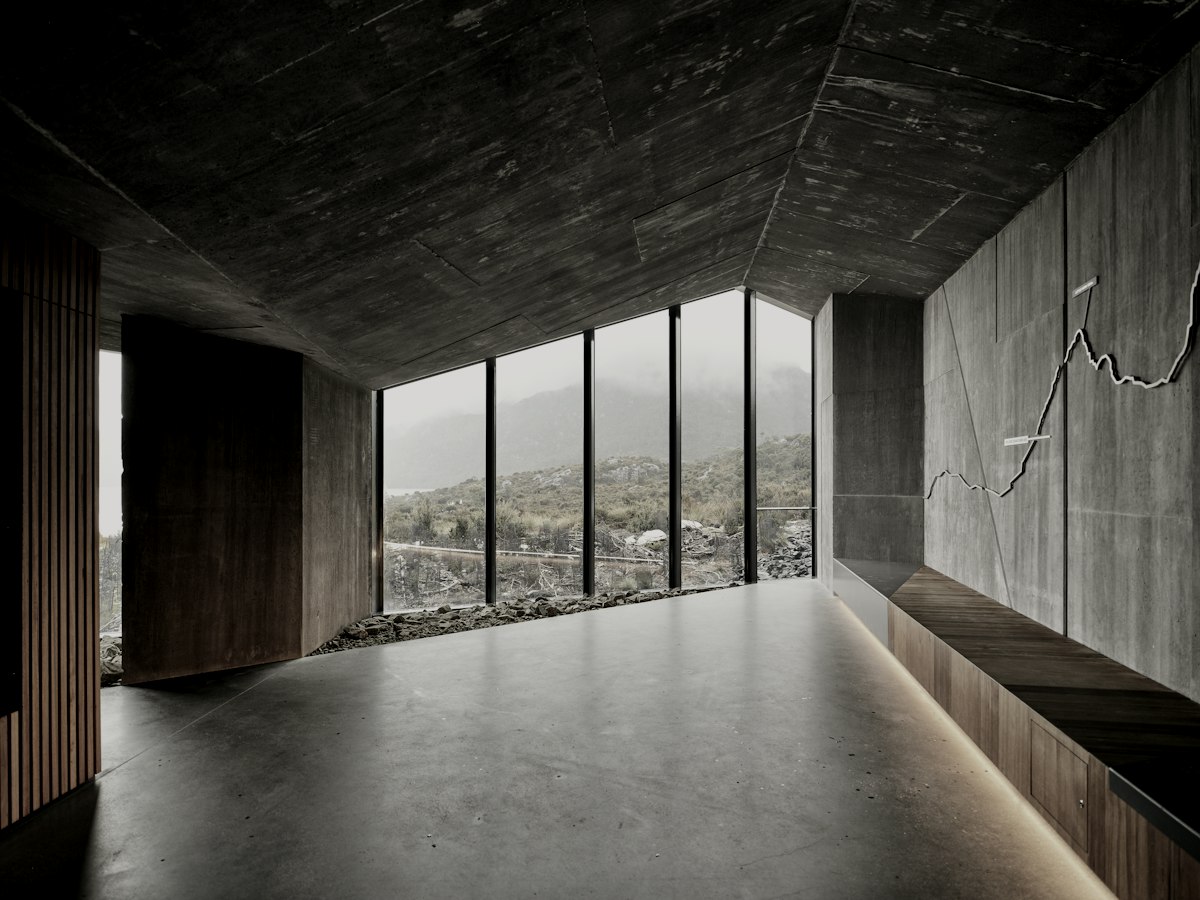 A long concrete room with a cedar door and a low window onto the mountains.