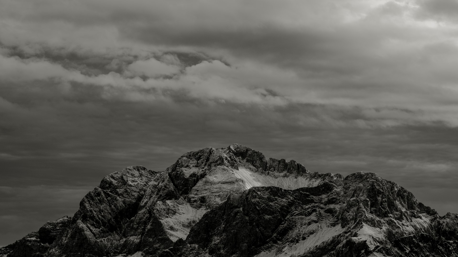 A rugged mountain peak under heavy cloud, in black and white.